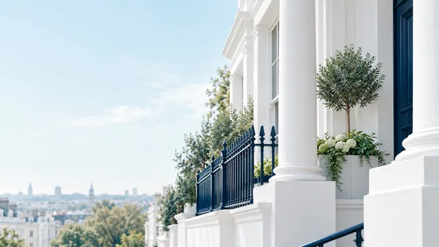 White stucco columns and navy railings beside a potted olive tree, with a pale sky and distant rooftops